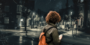 A woman on her phone looks down a dark street.
