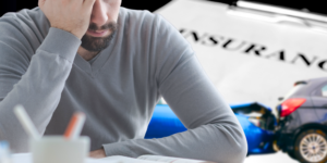Overwhelmed figure in front of a car wreck and large paper reading "INSURANCE."