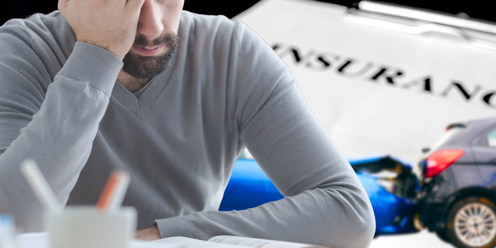 Overwhelmed figure in front of a car wreck and large paper reading "INSURANCE."